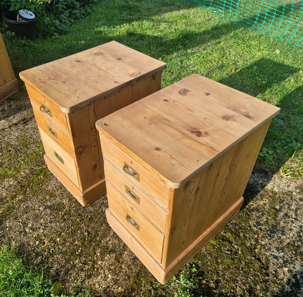 A pair of three-drawer natural pine bedside chests featuring brass flush campaign-style handles and solid plinth bases. View III