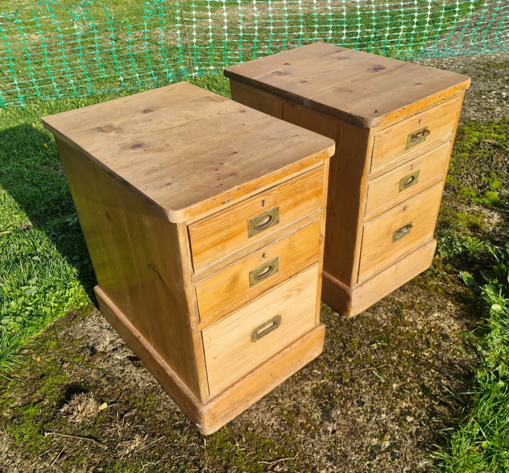 A pair of three-drawer natural pine bedside chests featuring brass flush campaign-style handles and solid plinth bases. View VI