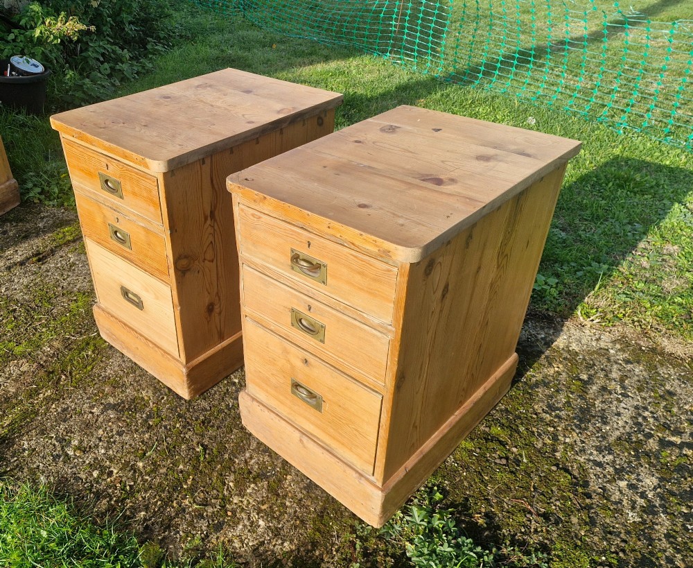 A pair of three-drawer natural pine bedside chests featuring brass flush campaign-style handles and solid plinth bases. View VIII