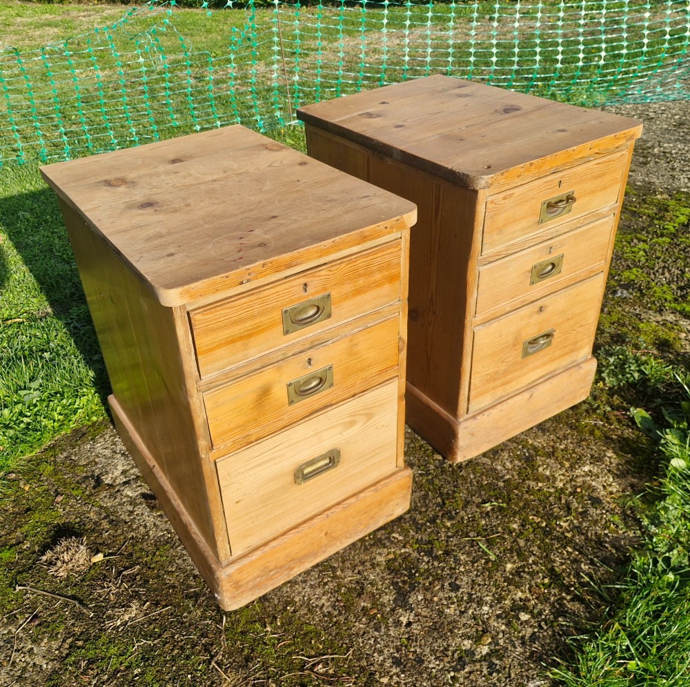 A pair of three-drawer natural pine bedside chests featuring brass flush campaign-style handles and solid plinth bases. View IX