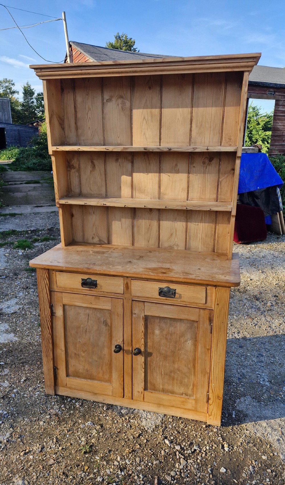 An early 20th-century natural pine kitchen dresser featuring a three-tier open shelf rack over two drawers and a two-door cabinet base. View V