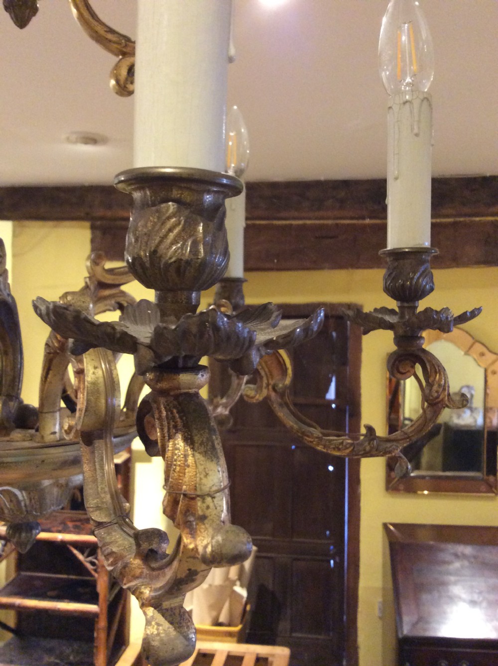 A nineteenth-century English gilt bronze chandelier featuring six scrolled arms, decorative foliate drip pans, and faux candle sleeves suspended from a central column. View II