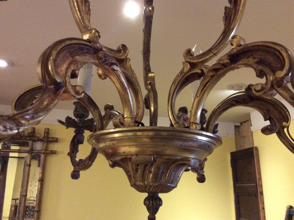 A nineteenth-century English gilt bronze chandelier featuring six scrolled arms, decorative foliate drip pans, and faux candle sleeves suspended from a central column. View III