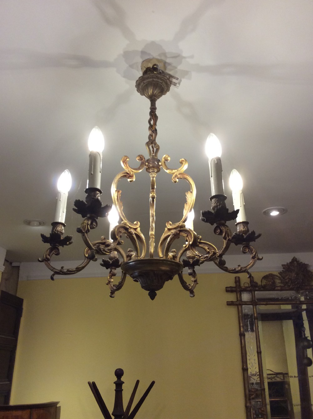 A nineteenth-century English gilt bronze chandelier featuring six scrolled arms, decorative foliate drip pans, and faux candle sleeves suspended from a central column. View V