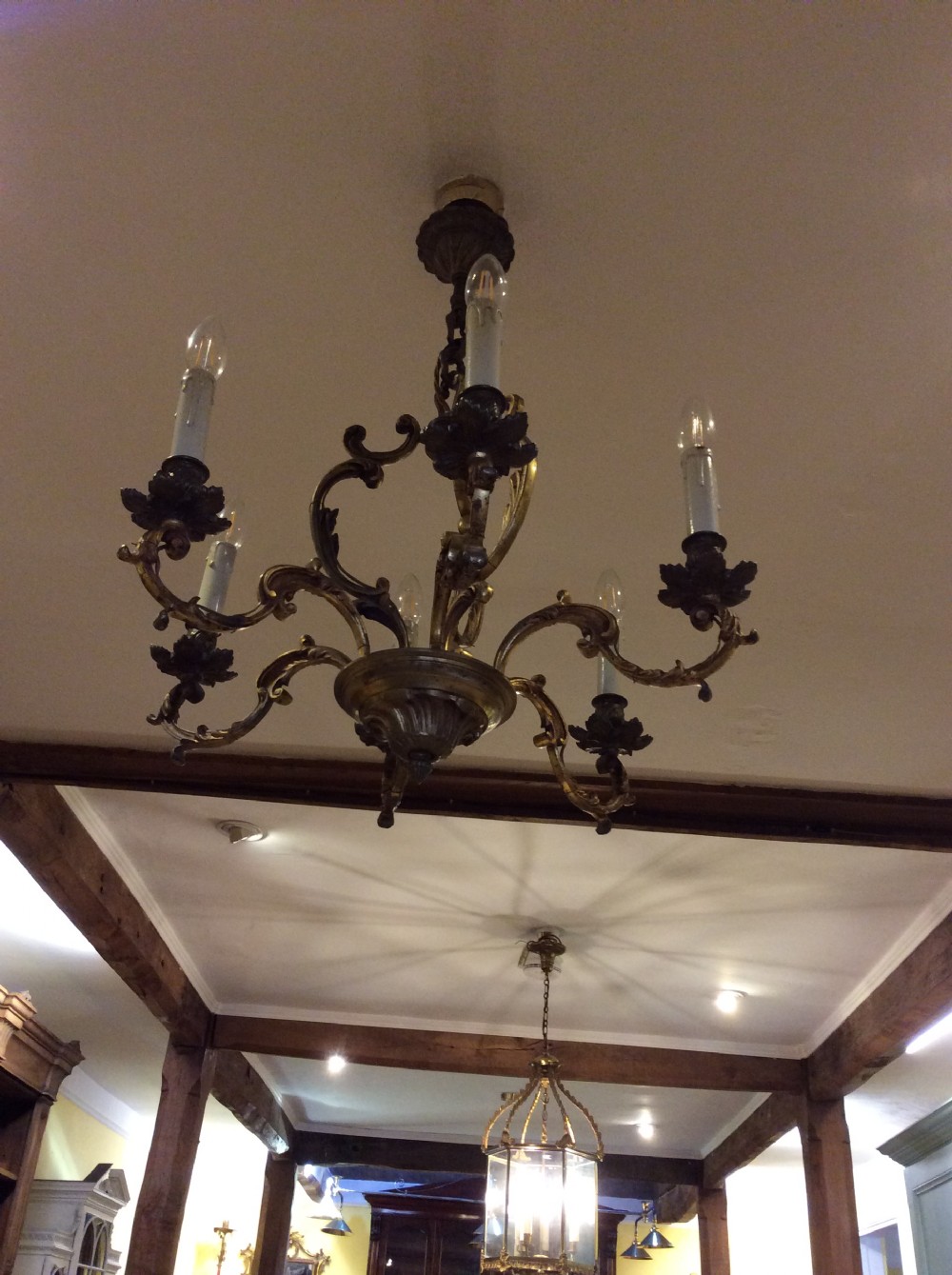 A nineteenth-century English gilt bronze chandelier featuring six scrolled arms, decorative foliate drip pans, and faux candle sleeves suspended from a central column. View VI