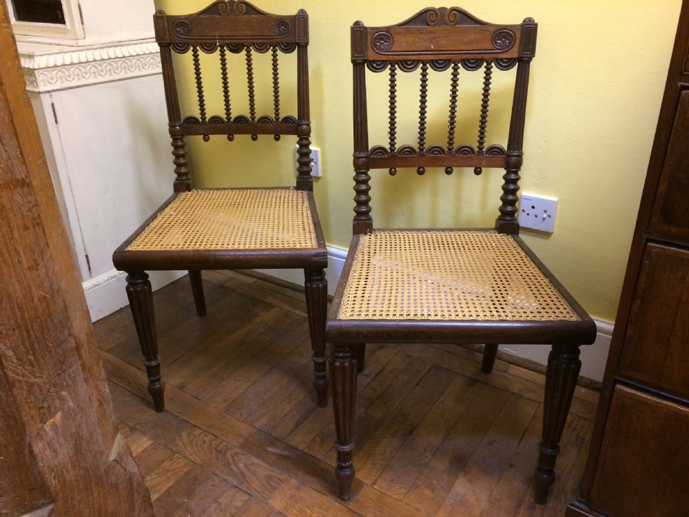 A pair of 19th-century carved dark rosewood side chairs featuring woven cane seats, spindle backrests, and fluted front legs.