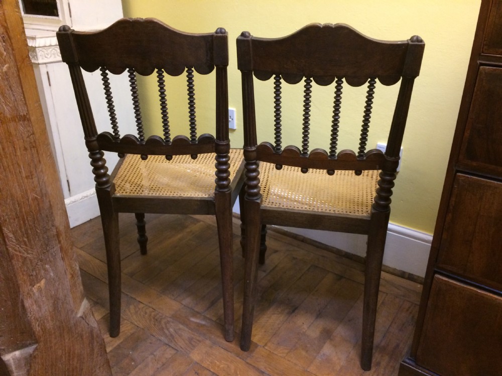 A pair of 19th-century carved dark rosewood side chairs featuring woven cane seats, spindle backrests, and fluted front legs. View V