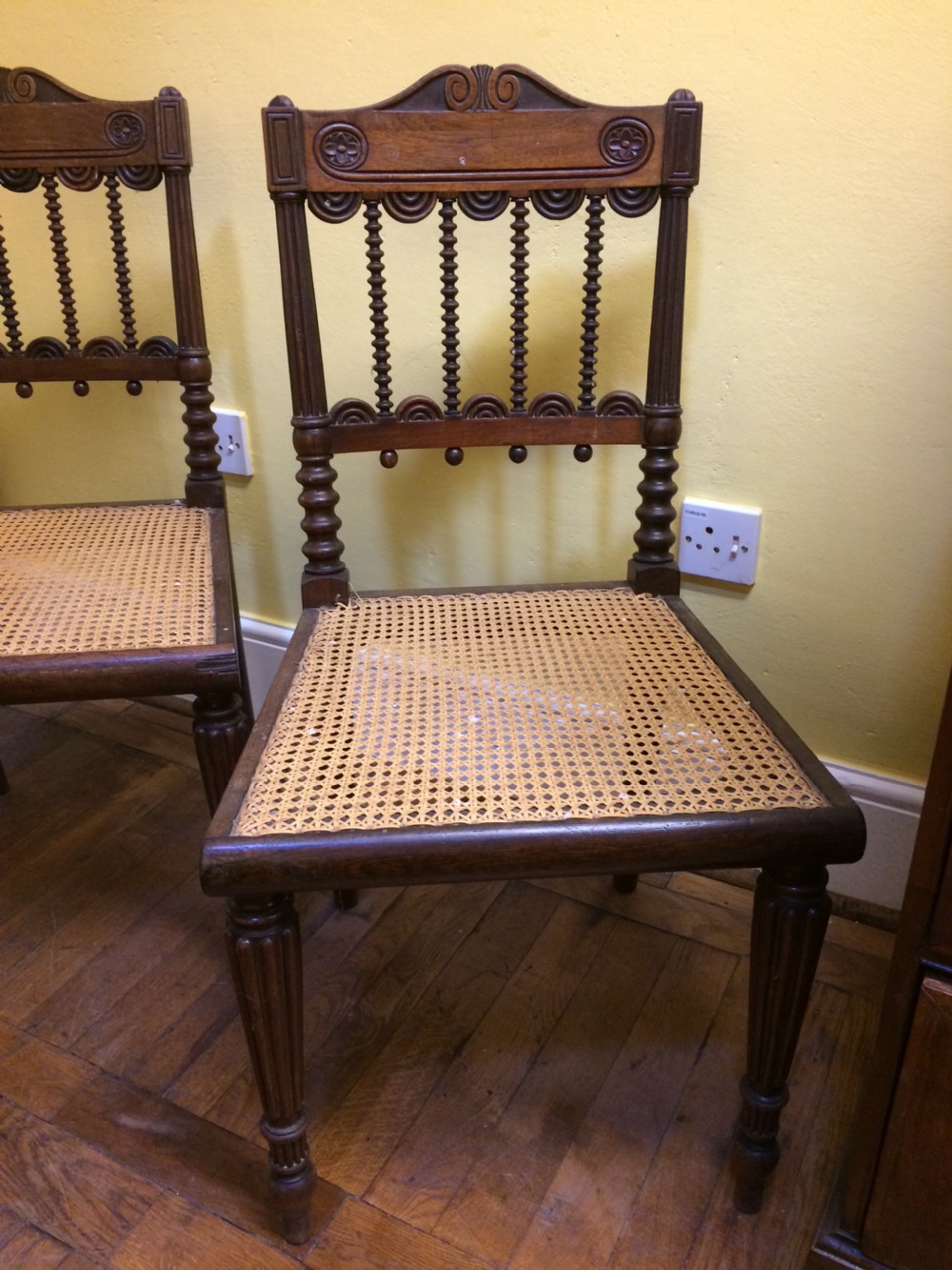 A pair of 19th-century carved dark rosewood side chairs featuring woven cane seats, spindle backrests, and fluted front legs. View VII