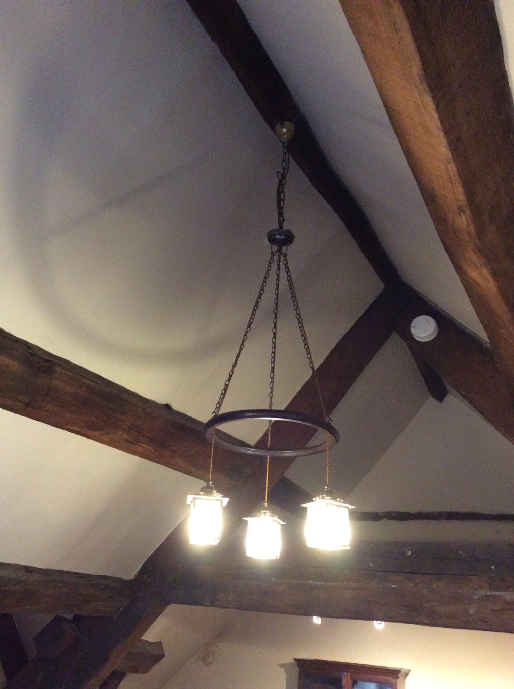 An Arts and Crafts style three-lantern ceiling light featuring a central circular dark frame suspended by chains with three hanging illuminated glass lanterns.