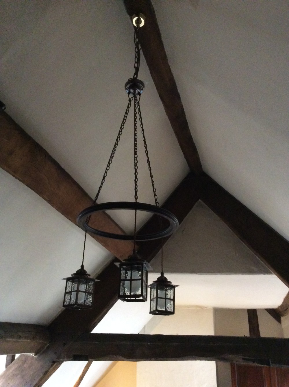 An Arts and Crafts style three-lantern ceiling light featuring a central circular dark frame suspended by chains with three hanging illuminated glass lanterns. View V