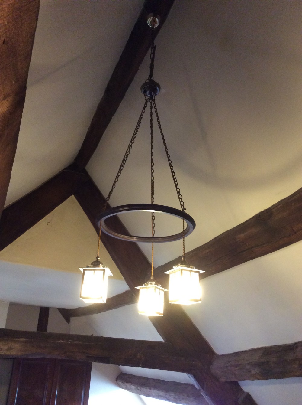 An Arts and Crafts style three-lantern ceiling light featuring a central circular dark frame suspended by chains with three hanging illuminated glass lanterns. View VI