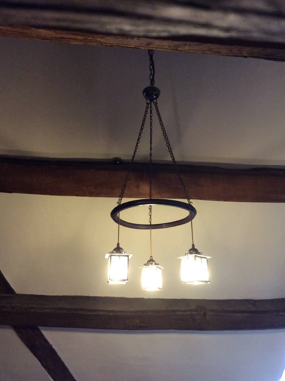 An Arts and Crafts style three-lantern ceiling light featuring a central circular dark frame suspended by chains with three hanging illuminated glass lanterns. View VIII