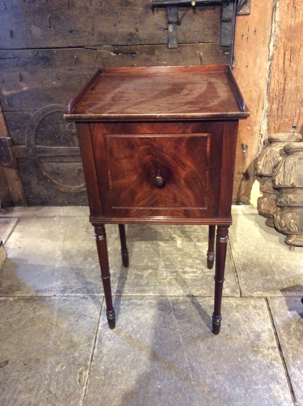 A Regency mahogany bedside cabinet featuring a gallery top, single flame mahogany door panel, and slender turned legs.