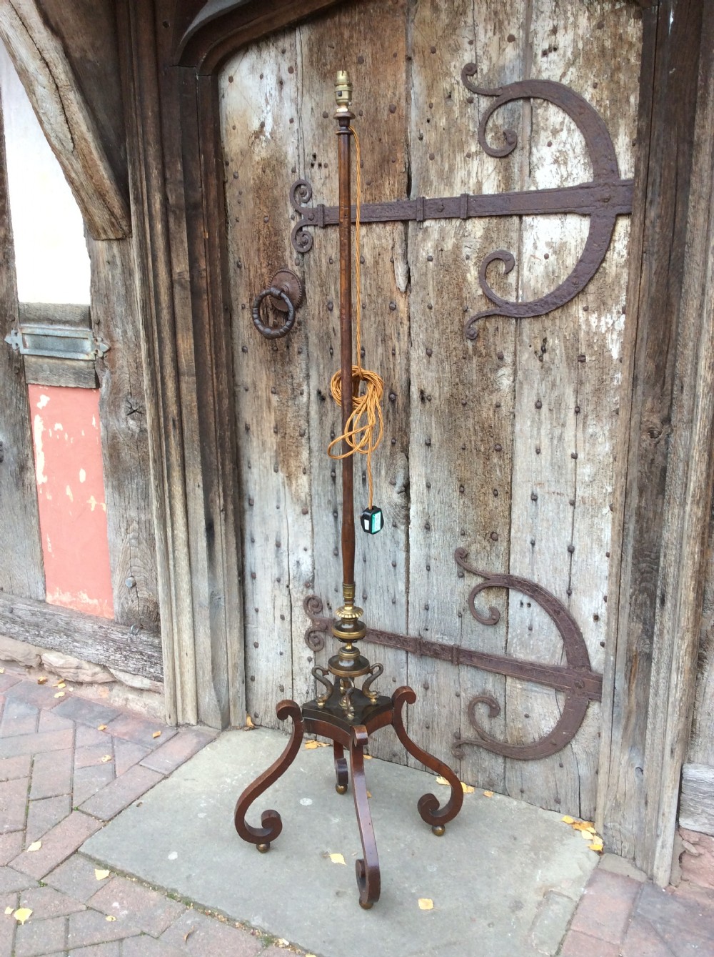 A 19th-century mahogany pole screen converted into a floor lamp featuring a slender turned shaft, gilt brass collars, and a scrolled tripod base.