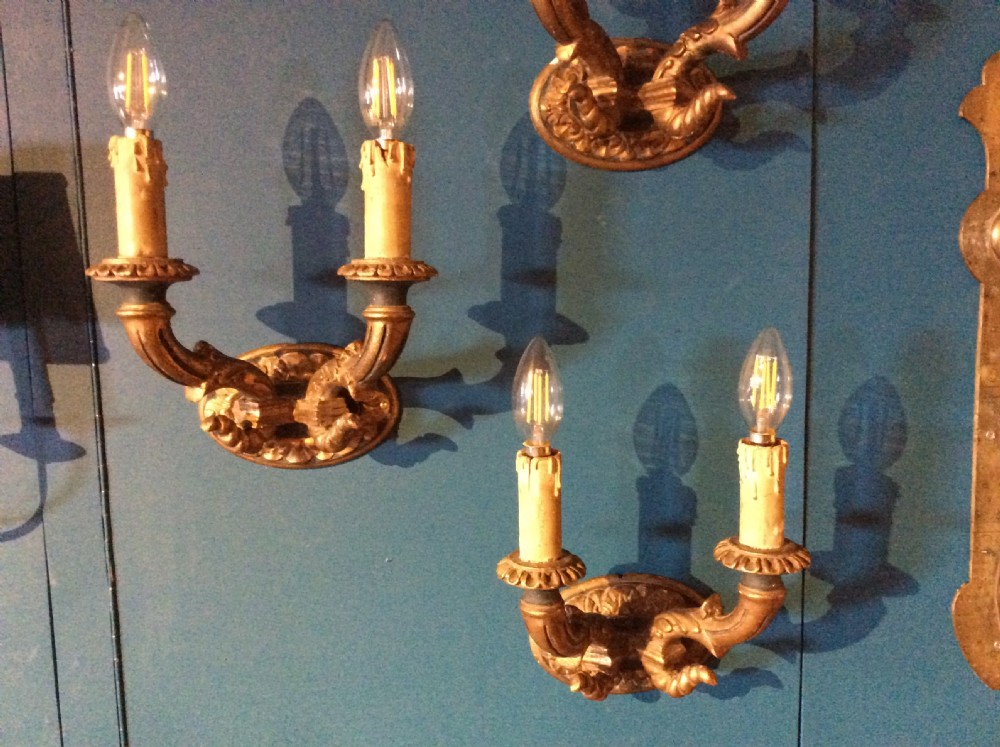 A pair of 19th-century carved gilt-wood twin-arm wall sconces featuring decorative candle sleeves and curved scroll arms mounted on oval backplates.