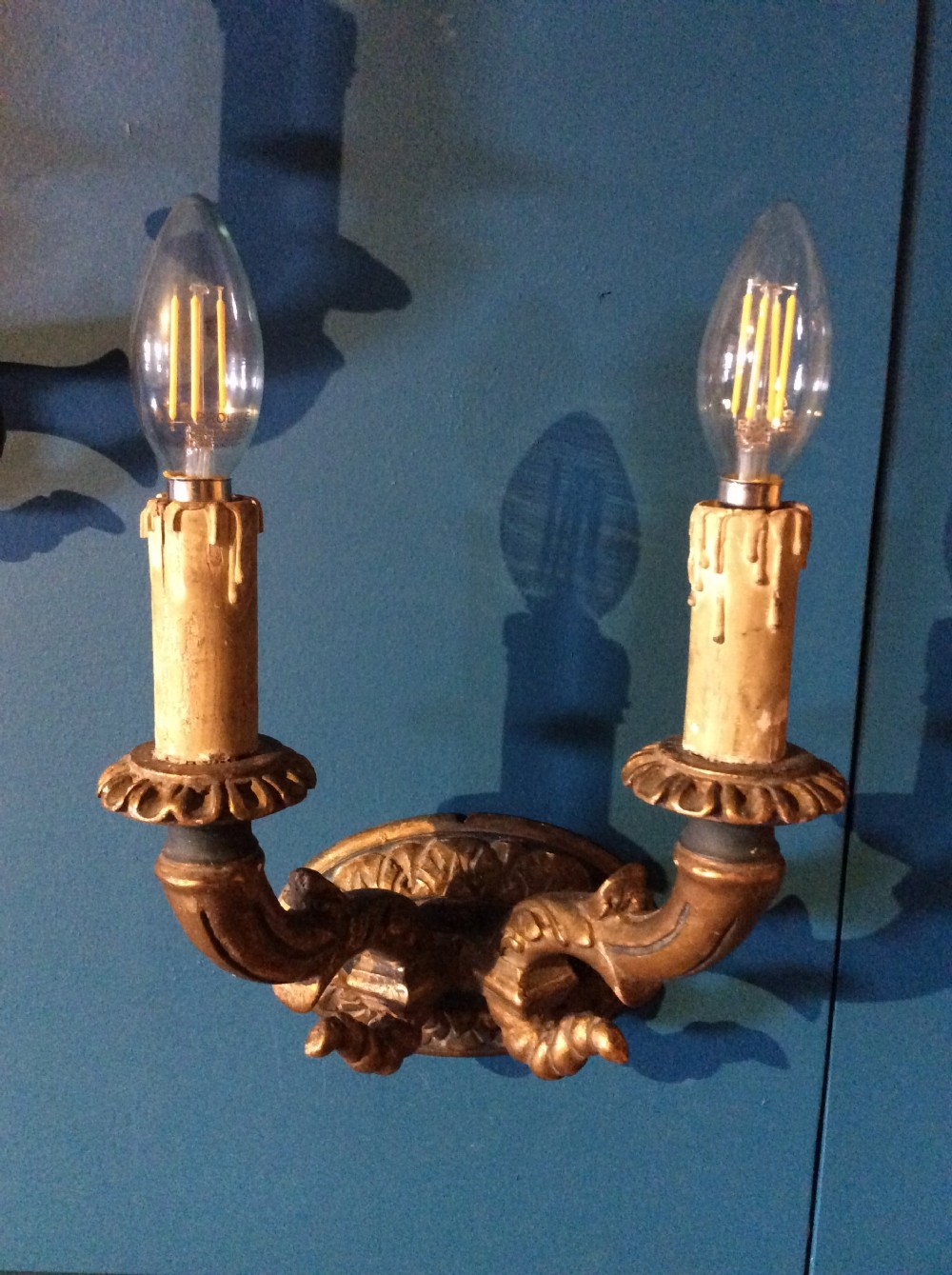 A pair of 19th-century carved gilt-wood twin-arm wall sconces featuring decorative candle sleeves and curved scroll arms mounted on oval backplates. View II