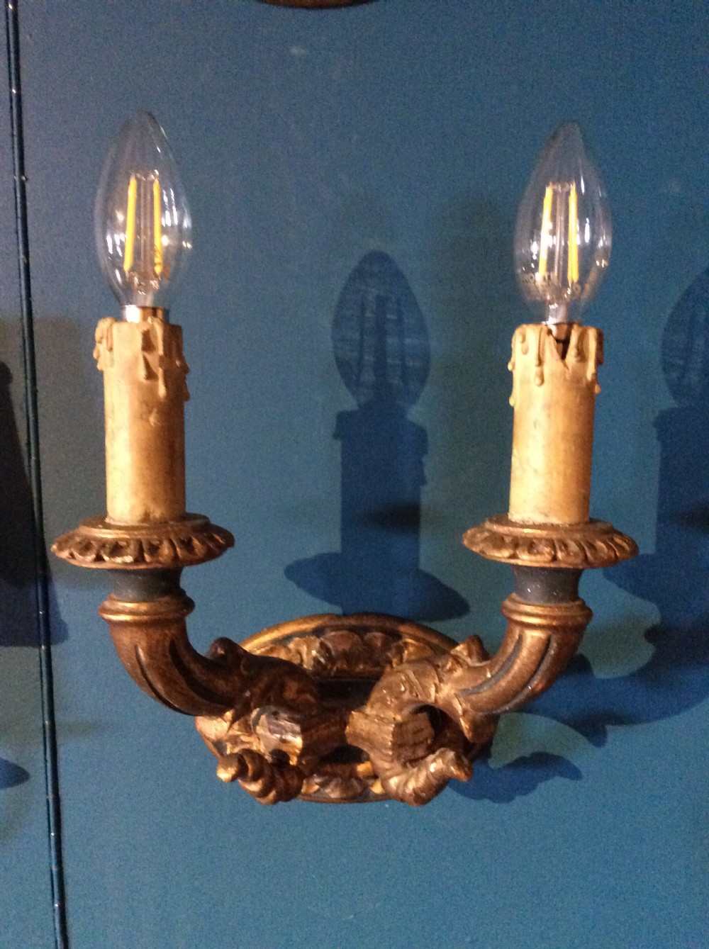 A pair of 19th-century carved gilt-wood twin-arm wall sconces featuring decorative candle sleeves and curved scroll arms mounted on oval backplates. View III