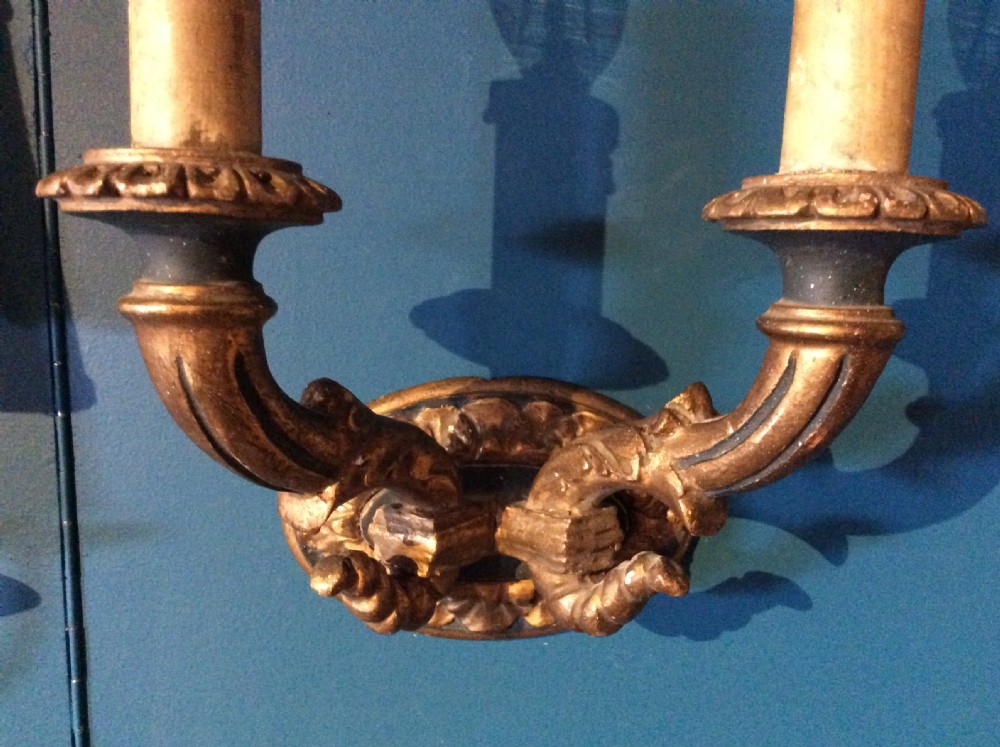 A pair of 19th-century carved gilt-wood twin-arm wall sconces featuring decorative candle sleeves and curved scroll arms mounted on oval backplates. View IV