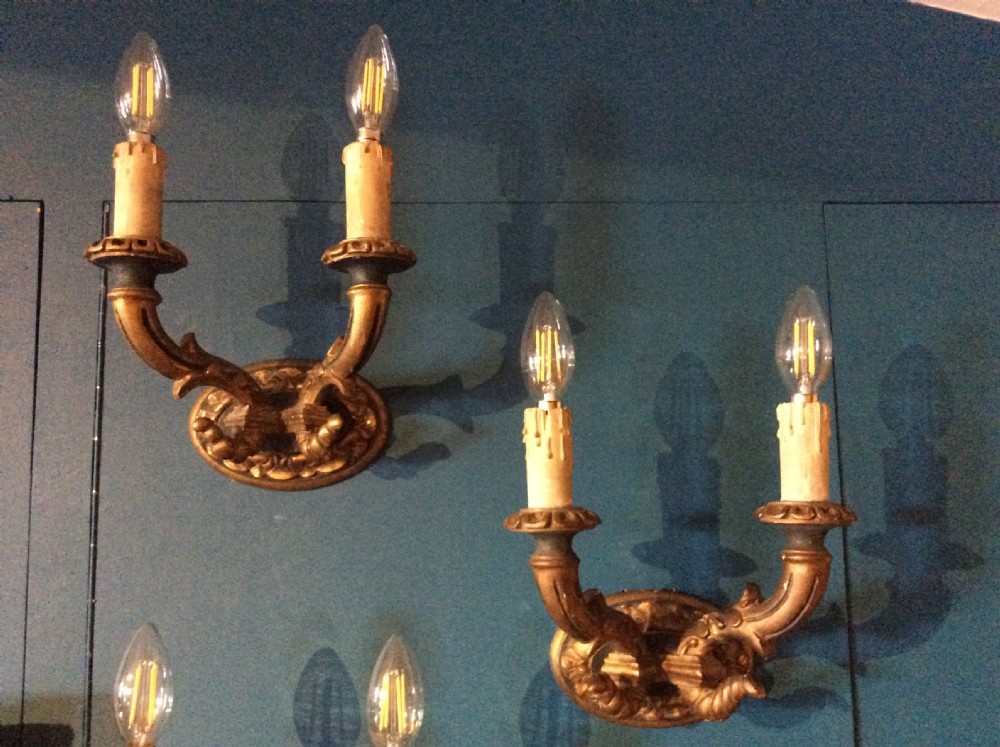 A pair of 19th-century carved and gilded twin-arm wall light brackets featuring faux candle sleeves and decorative scrollwork.