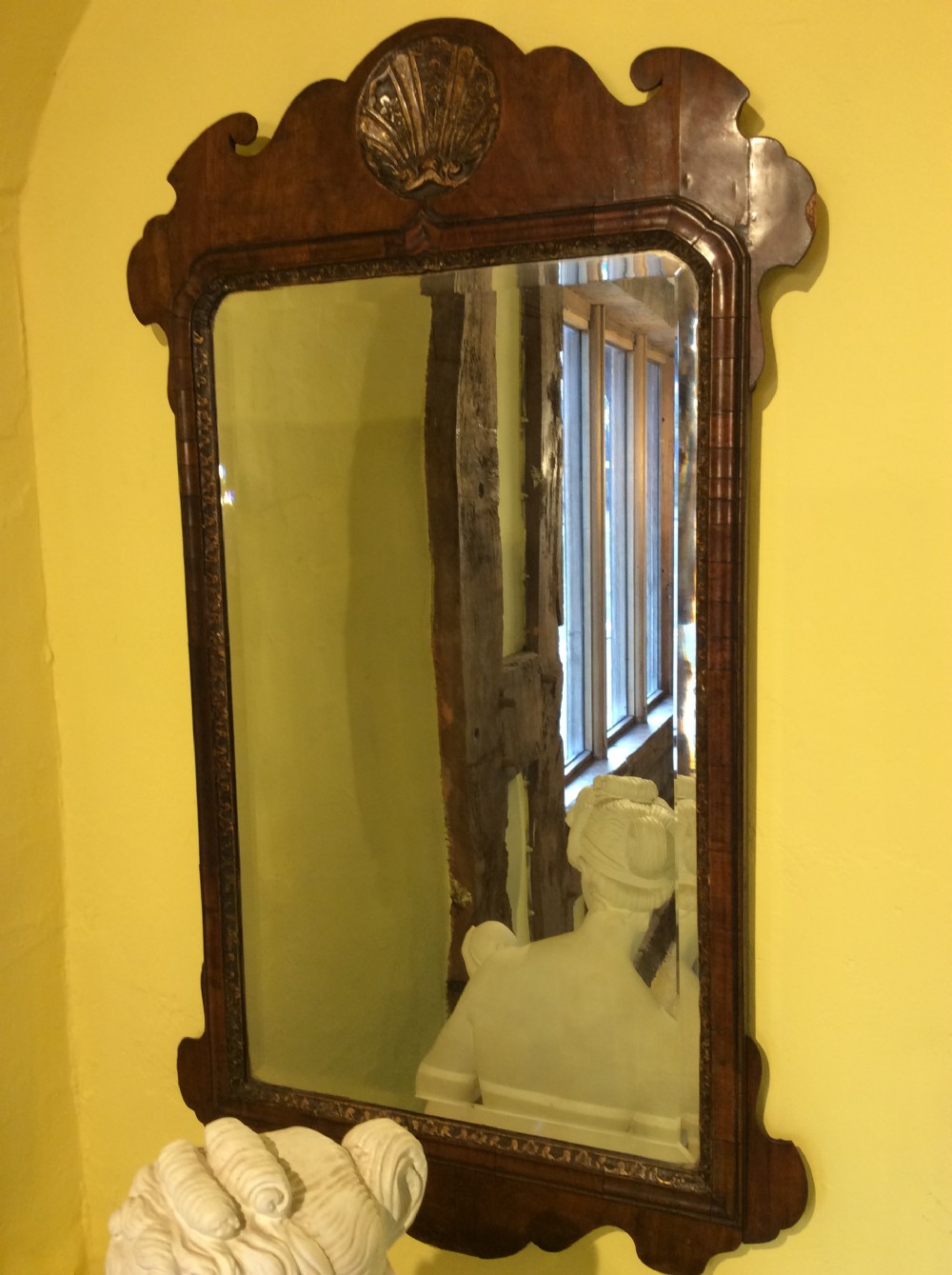 An 18th-century Queen Anne walnut wall mirror featuring a scroll-cut shaped apron and top cresting adorned with a carved gilt shell.