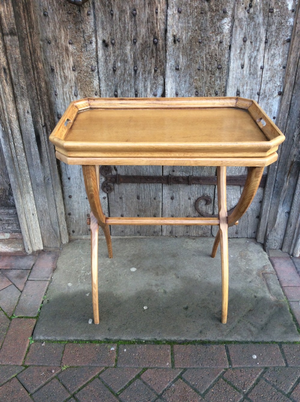 An early twentieth-century light oak butlers tray featuring cut-out handles, resting on a matching curved wooden stand.