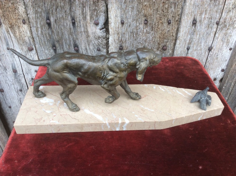 A dark bronze sculpture depicting a hunting dog stalked towards a small bird, mounted on a cream marble plinth. View II