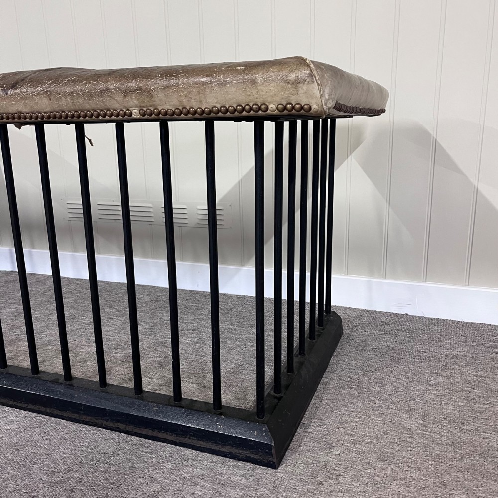 A nineteenth-century steel club fender with vertical black spindles, a solid base frame, and a tan leather upholstered rim trimmed with brass studs. View II