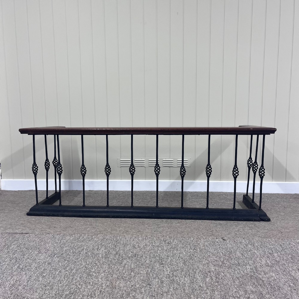 A 19th-century club fender featuring a polished mahogany top rail supported by black wrought iron twisted spindles on a low plinth base.
