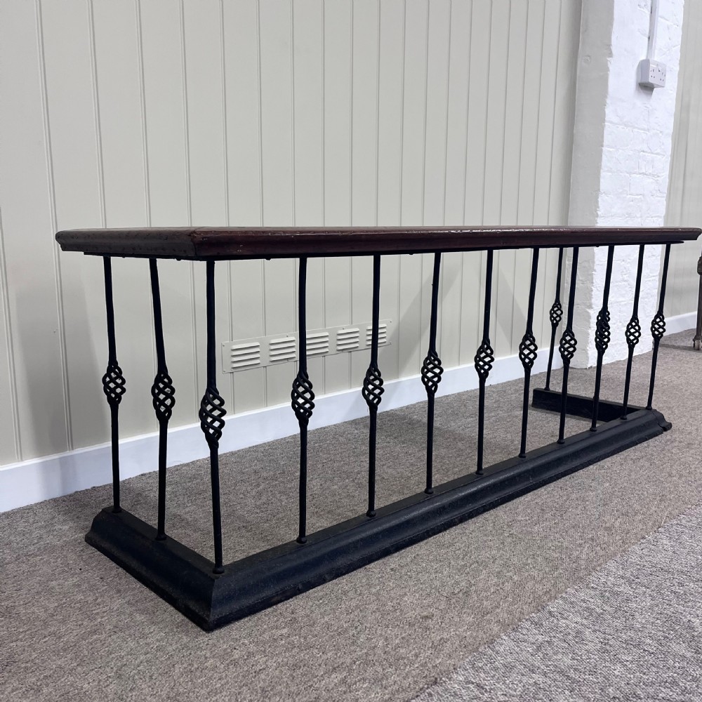 A 19th-century club fender featuring a polished mahogany top rail supported by black wrought iron twisted spindles on a low plinth base. View II