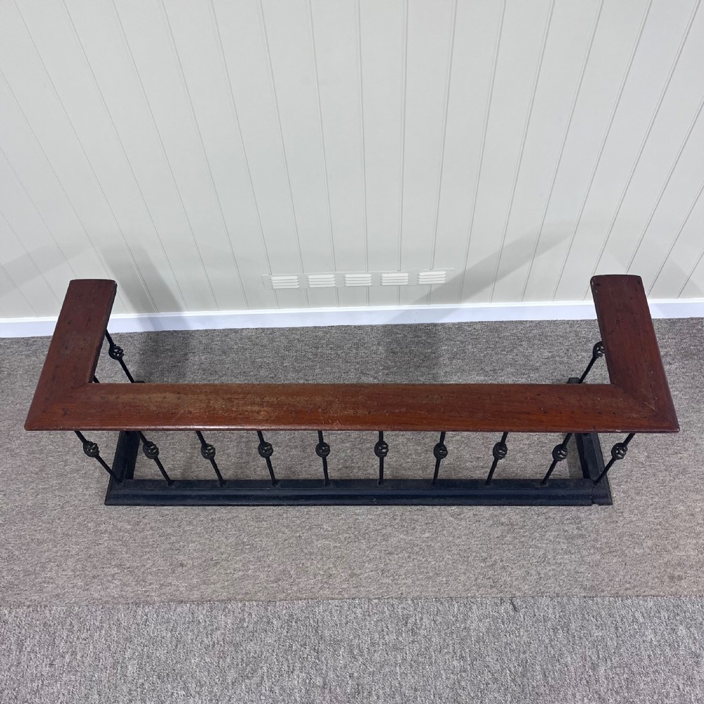 A 19th-century club fender featuring a polished mahogany top rail supported by black wrought iron twisted spindles on a low plinth base. View III