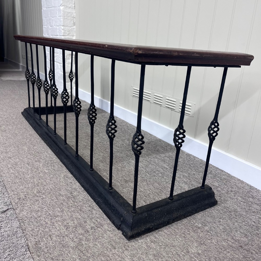 A 19th-century club fender featuring a polished mahogany top rail supported by black wrought iron twisted spindles on a low plinth base. View IV