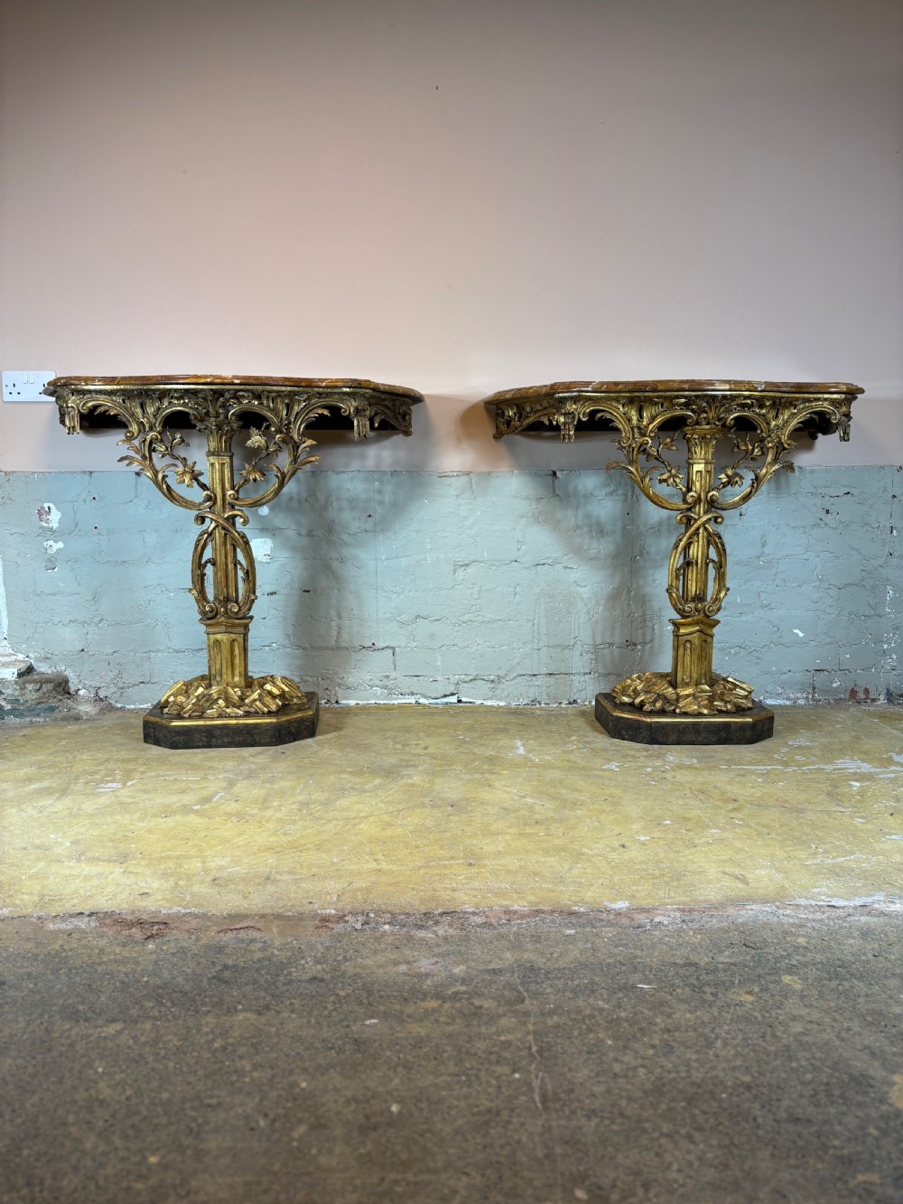 A pair of 18th-century carved giltwood side tables with openwork scrolling pedestal bases and marble tops.