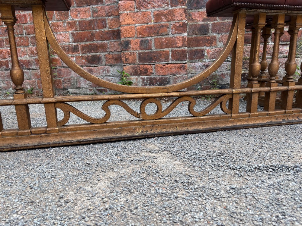 A 19th-century cast steel club fender with turned balusters, decorative lower scrollwork, and two corner seats upholstered in deep-buttoned burgundy leather with metal stud trim. View IV