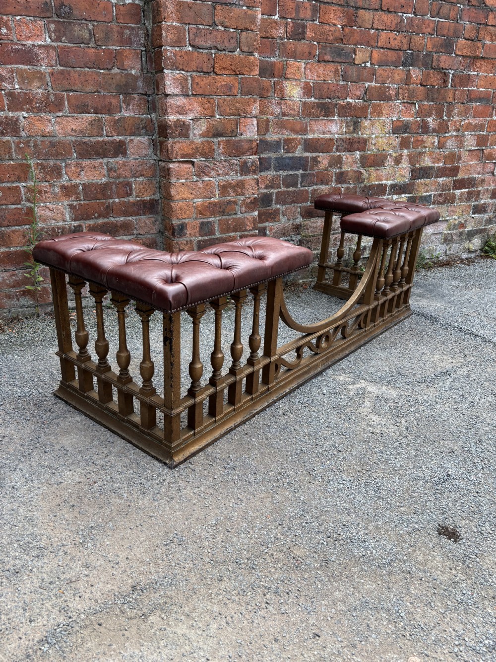 A 19th-century cast steel club fender with turned balusters, decorative lower scrollwork, and two corner seats upholstered in deep-buttoned burgundy leather with metal stud trim. View V