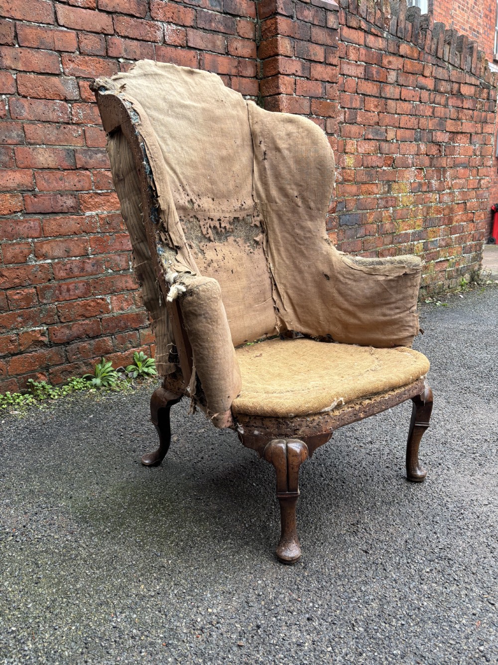 An 18th century Queen Anne wing armchair frame in worn hessian fabric with carved walnut cabriole front legs. View II