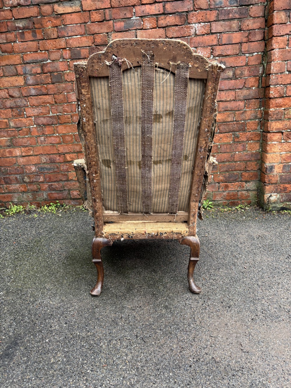 An 18th century Queen Anne wing armchair frame in worn hessian fabric with carved walnut cabriole front legs. View IV