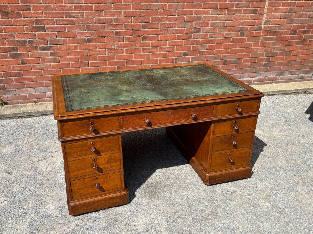 A 19th-century oak partners desk featuring a green leather inset top, two pedestals with multiple drawers, and carved wooden handles.
