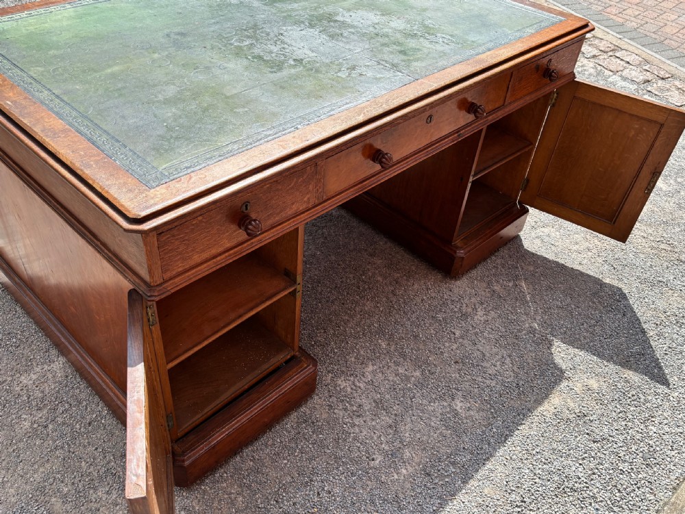 A 19th-century oak partners desk featuring a green leather inset top, two pedestals with multiple drawers, and carved wooden handles. View IV
