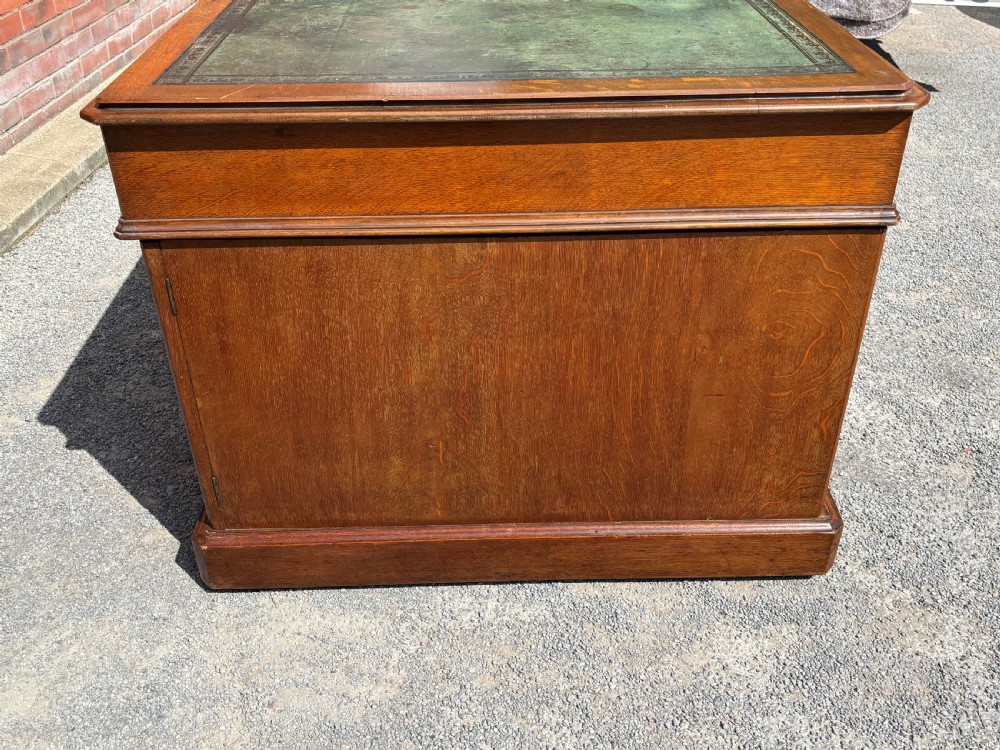 A 19th-century oak partners desk featuring a green leather inset top, two pedestals with multiple drawers, and carved wooden handles. View V
