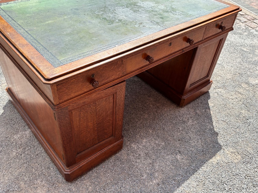 A 19th-century oak partners desk featuring a green leather inset top, two pedestals with multiple drawers, and carved wooden handles. View VI
