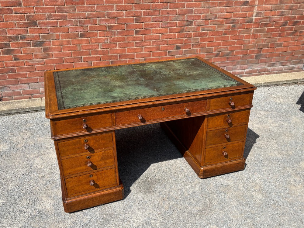 A 19th-century oak partners desk featuring a green leather inset top, two pedestals with multiple drawers, and carved wooden handles. View X
