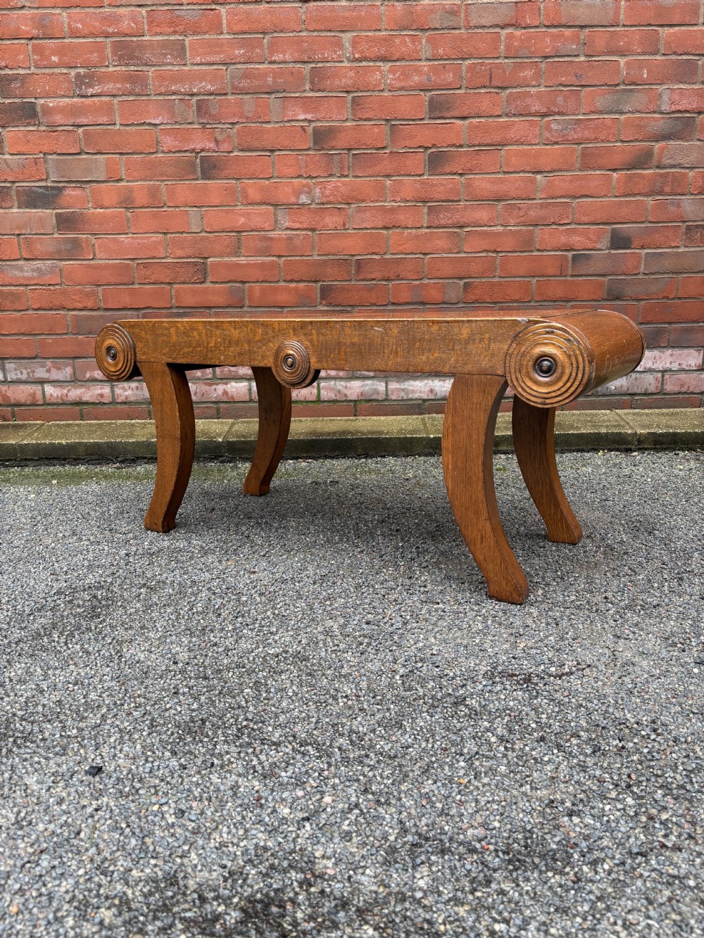 A Regency style oak hall bench featuring rolled scroll ends with central roundel carvings and outwardly curved sabre legs.