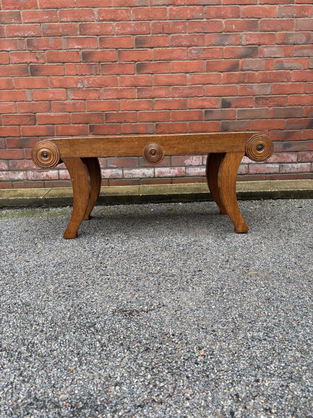 A Regency style oak hall bench featuring rolled scroll ends with central roundel carvings and outwardly curved sabre legs. View II