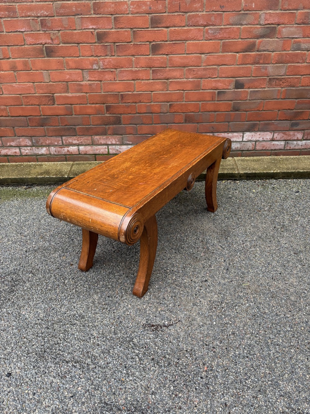 A Regency style oak hall bench featuring rolled scroll ends with central roundel carvings and outwardly curved sabre legs. View IV