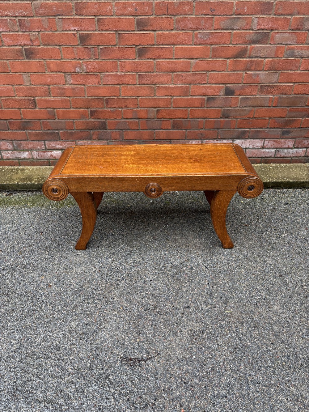 A Regency style oak hall bench featuring rolled scroll ends with central roundel carvings and outwardly curved sabre legs. View V