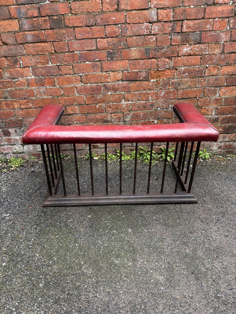 An antique 19th-century steel club fender featuring a red leather padded top seat supported by vertical steel spindles on a moulded metal base. View IV
