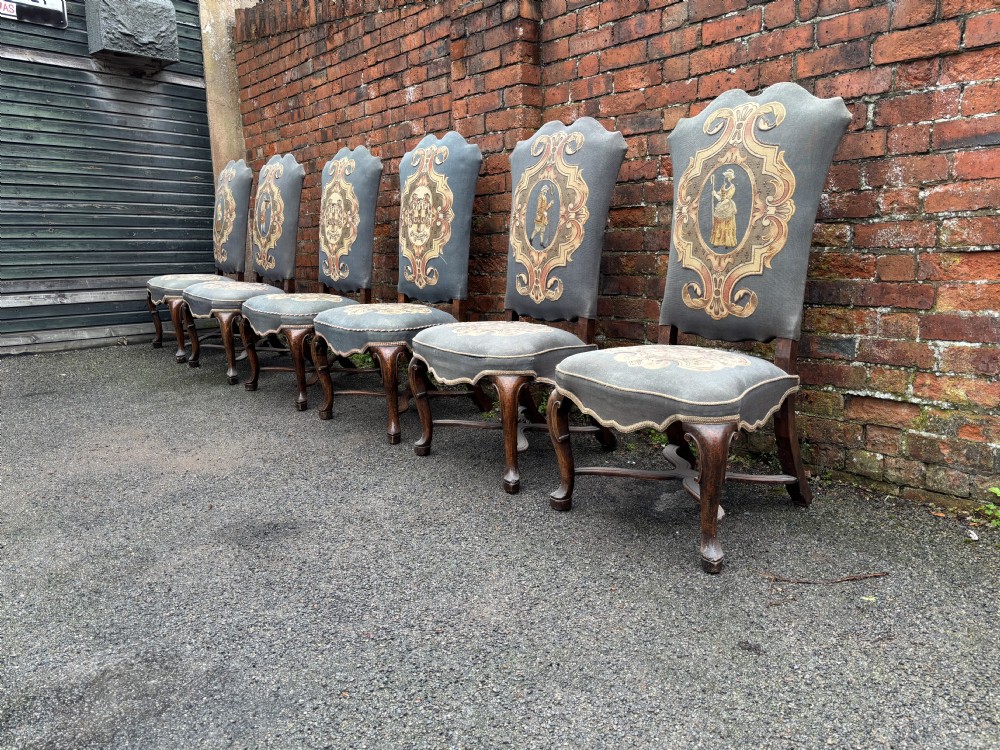 A set of six 18th-century Italian walnut dining chairs with tall backrests upholstered in grey fabric featuring central embroidered figural panels and cabriole legs.