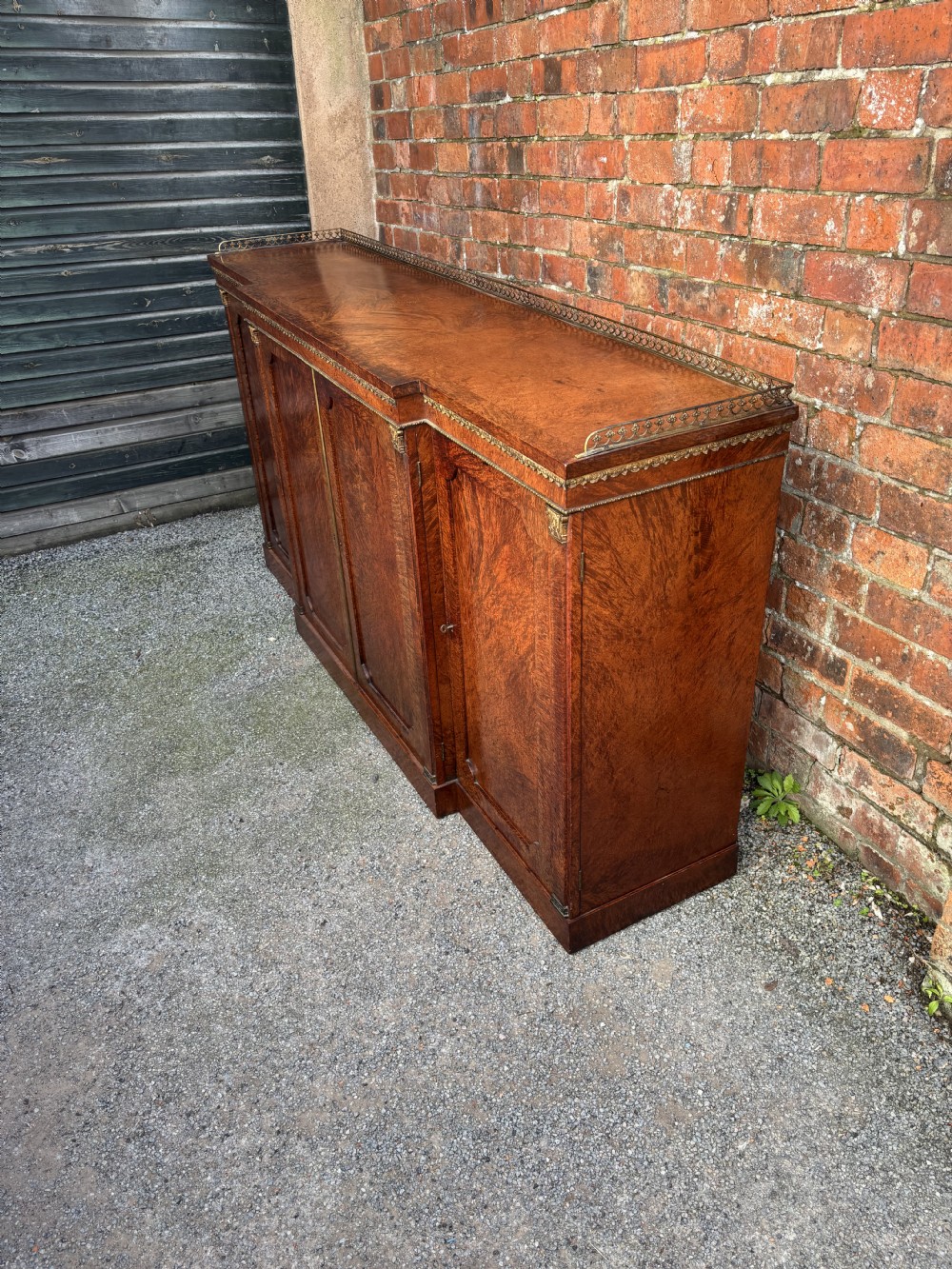 A low Regency period side cabinet crafted from figured brown amboyna wood veneer with a pierced brass gallery rail and panelled cupboard doors.