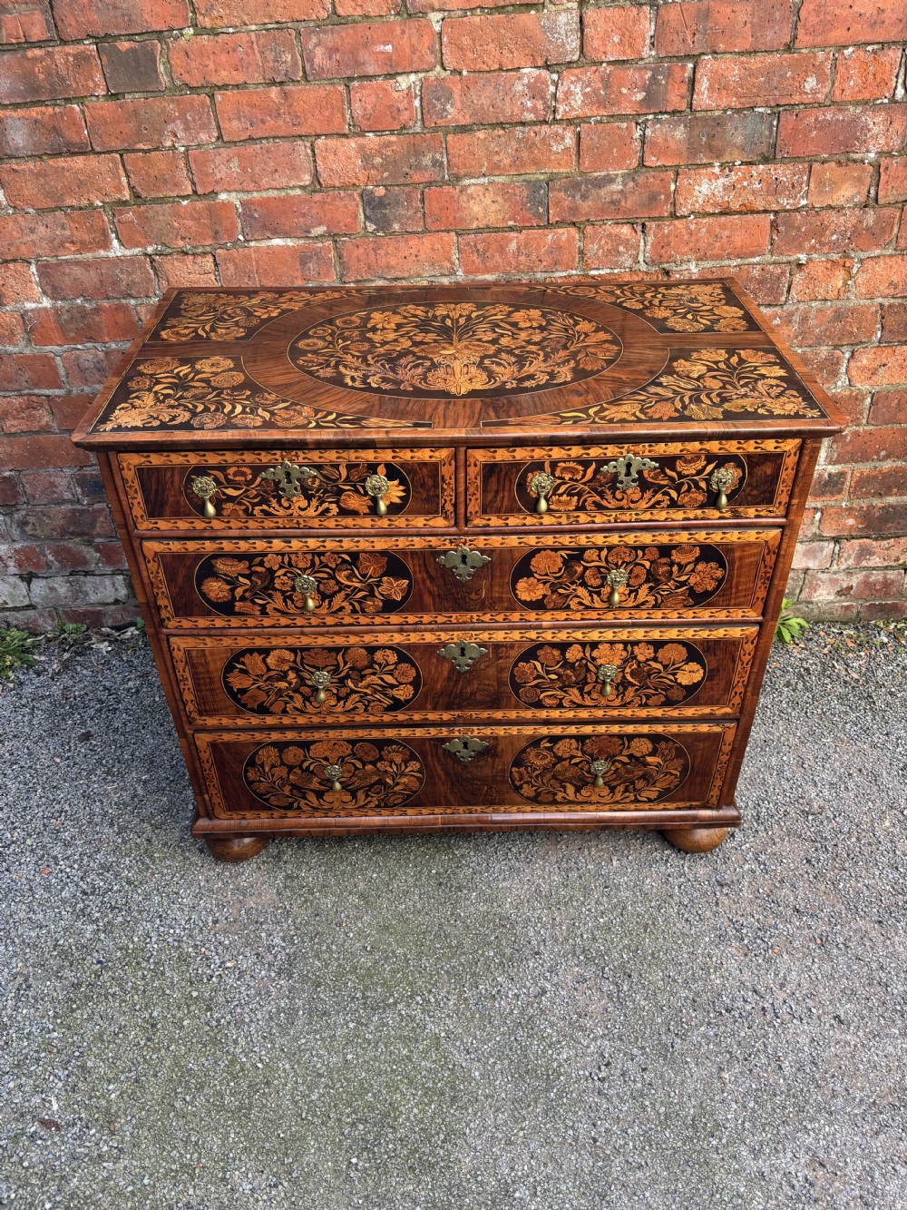 A 17th-century walnut chest of drawers featuring floral marquetry panels, teardrop brass drop handles, and turned bun feet. View III