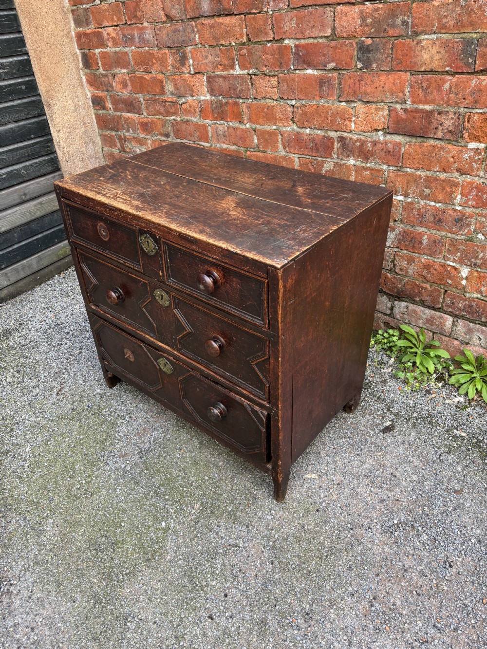 A dark oak 17th-century chest of drawers featuring geometric moulded drawer fronts, turned wooden handles, and brass escutcheons. View II